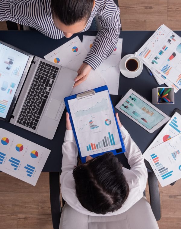Top viewTop view of manager and employee doing teamwork in business office , looking at charts on laptop display. Finance paperwork with charts at workplace. Discusing financial plan.